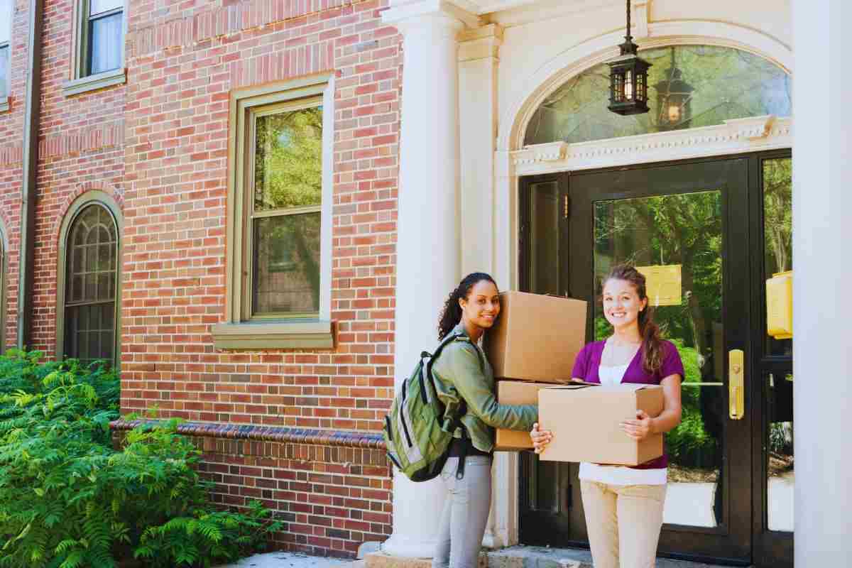 due studentesse davanti a una casa con gli scatoloni