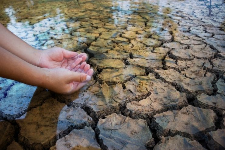 Le mani di una bambina che tenta di prendere acqua da un corso d'acqua, ma c'è siccità