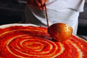 pizzaiolo mette sugo sulla pizza