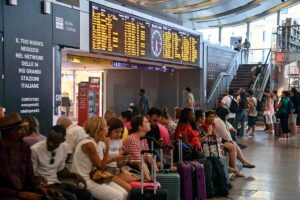 Persone sedute alla stazione con valigia al seguito