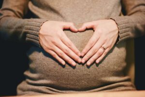 Una futura mamma fa con le mani la forma del cuore sul pancione