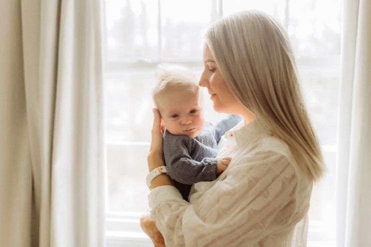 Una mamma tiene in braccio il figlio piccolo accanto a una finestra