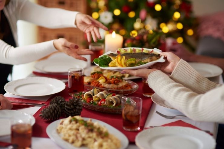 Due commensali si passano un piatto di pesce a Natale