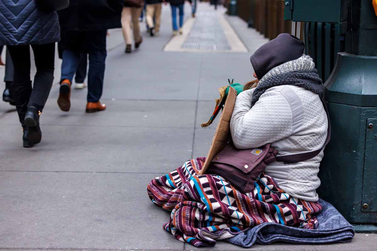 Clochard seduta in strada, su un marciapiede