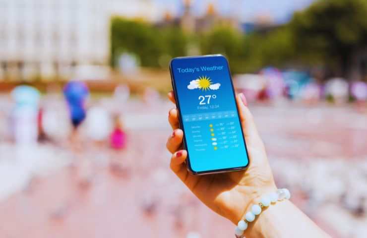 sole e la mano di una ragazza con uno smartphone che mostra il meteo