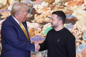 Sullo sfondo, i minerali, in primo piano Donald Trump e Volodymyr Zelensky mentre si stringono la mano