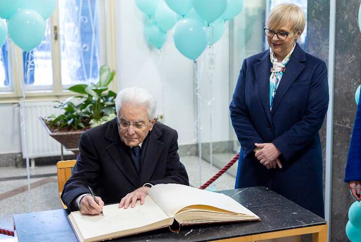 mattarella seduto firma un verbale al fianco di una donna in piedi vicino a lui