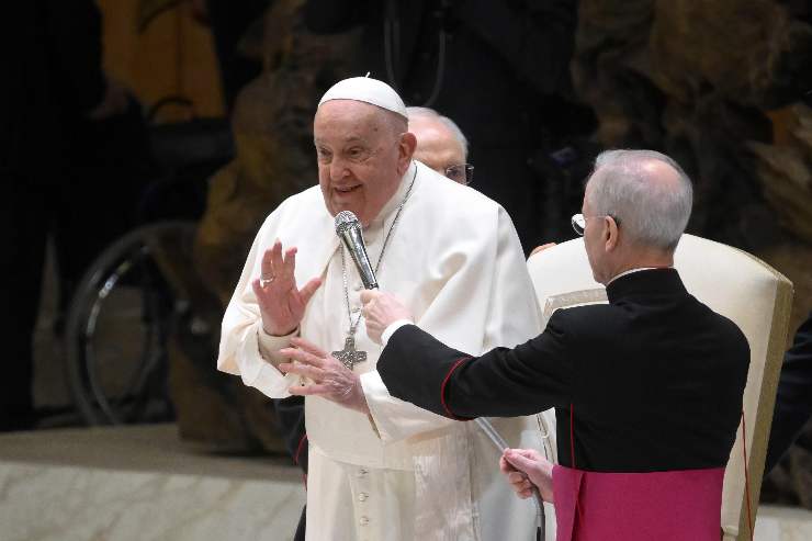 papa francesco parla in piedi al microfono aiutato da un vescovo