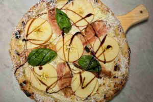 una pizza con mela speck e basilico su un tagliere di legno