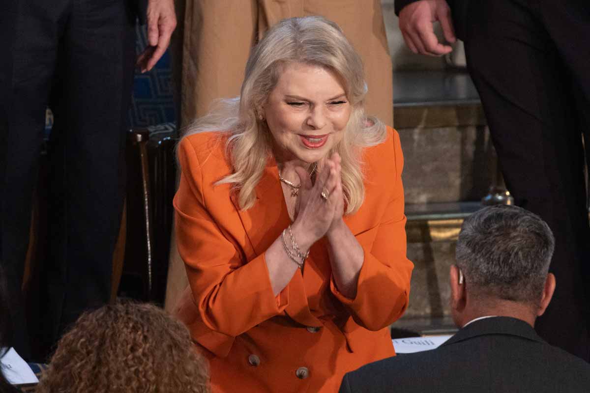 Sara Netanyahu con le mani giunge, in vestito arancione