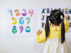 Bambina con camicetta gialla, di spalle, che studia le lettere dell'alfabeto