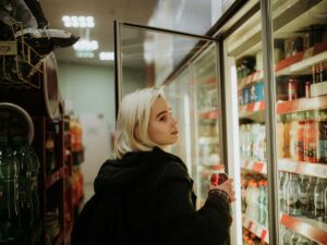 Una ragazza bionda in un supermercato che apre un frigo per prendere una bibita